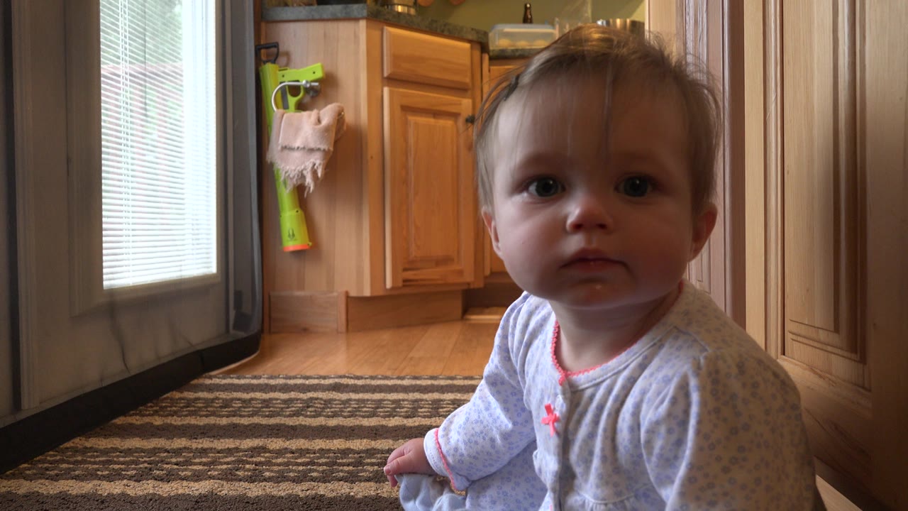 Baby sitting on a kitchen floor near cabinets and a glass door.