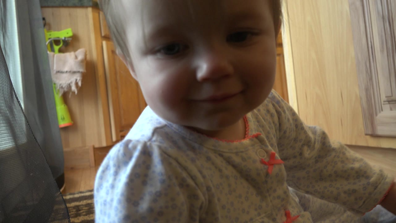 The baby remains close to camera with a small smile, the highchair mesh at frame left and warm wood cabinetry in the Westminster, Colorado kitchen background.