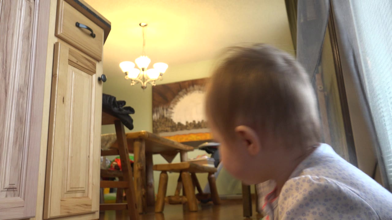 Toddler beside a curtain in a living room.