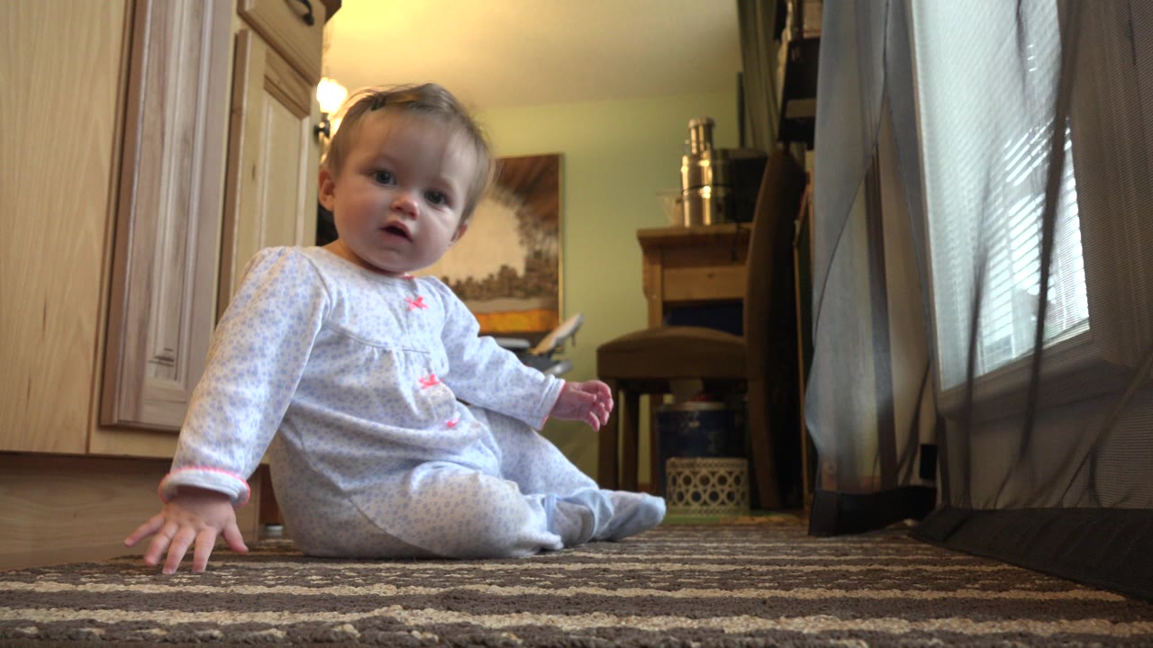 Baby sitting on a patterned rug in a home interior.