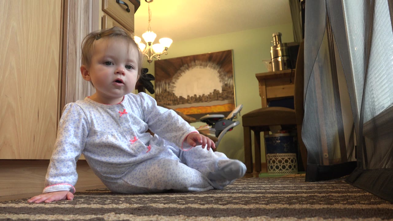 Baby girl seated with her legs forward on a living room carpet.