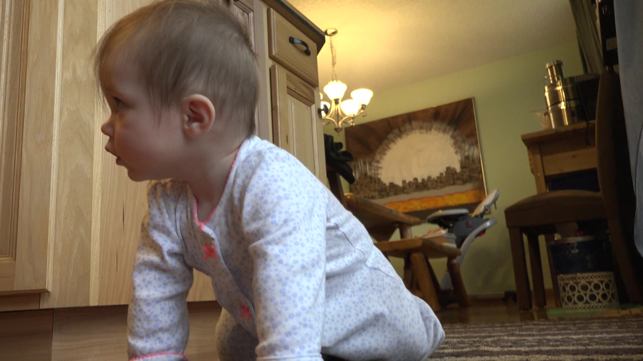 Baby in profile crawling beside kitchen cabinets.