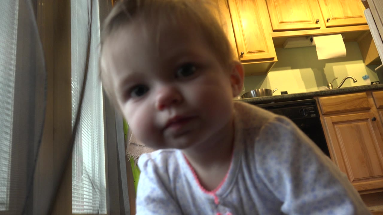 Baby girl close to a low camera in a kitchen.