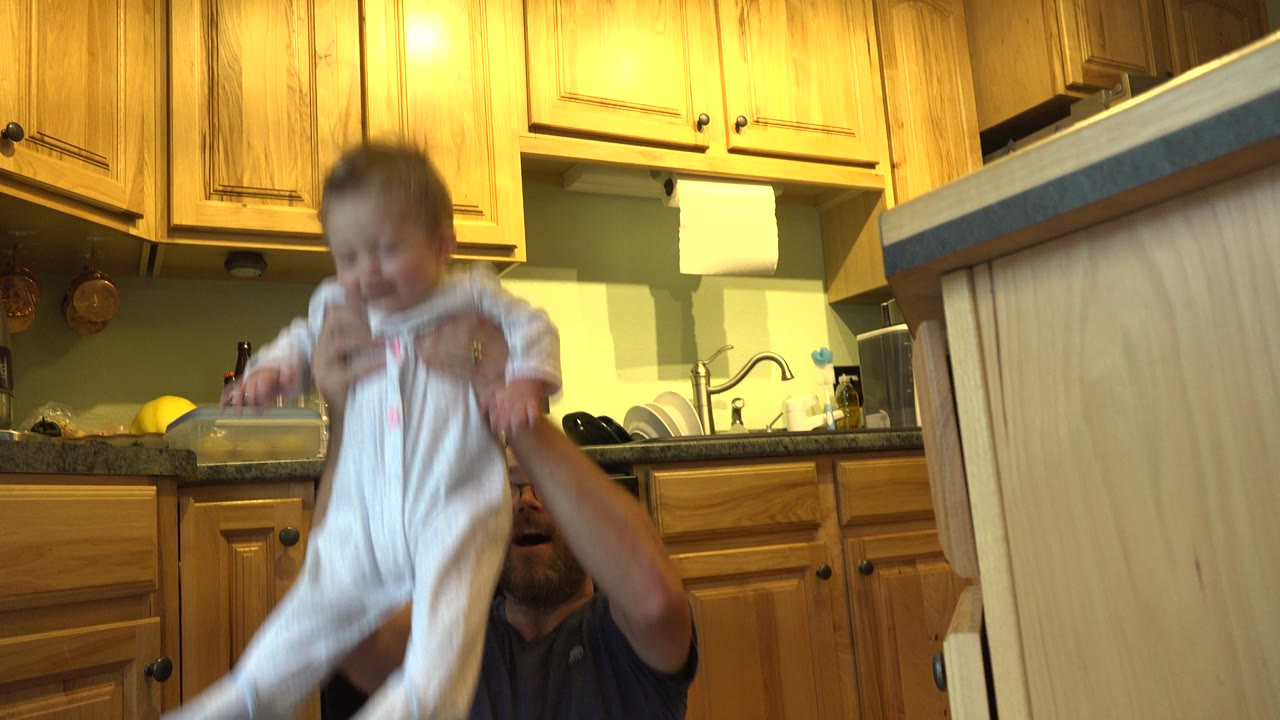Father lifting a toddler in a warm kitchen.