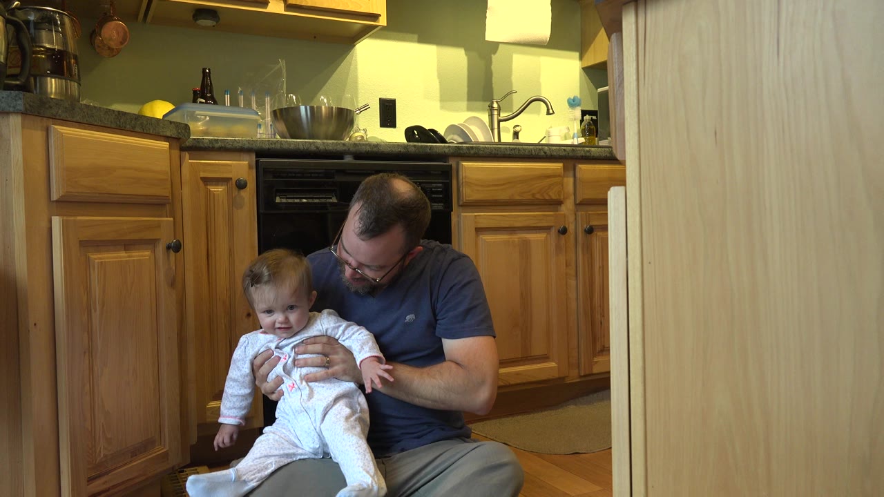 Father holding baby on a kitchen floor.