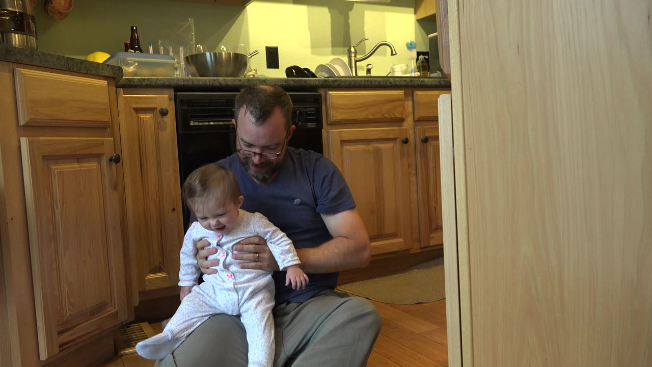 Father seated with baby on his lap in kitchen.