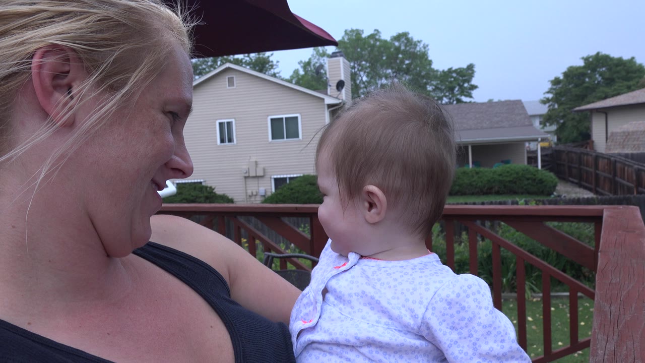 Mother holds baby daughter on a backyard deck.