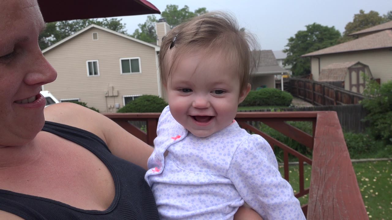Mother holding a smiling baby on a backyard deck.