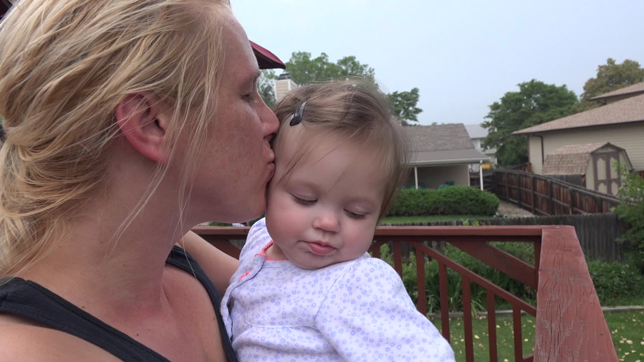 Woman kisses a baby on the head in a backyard.