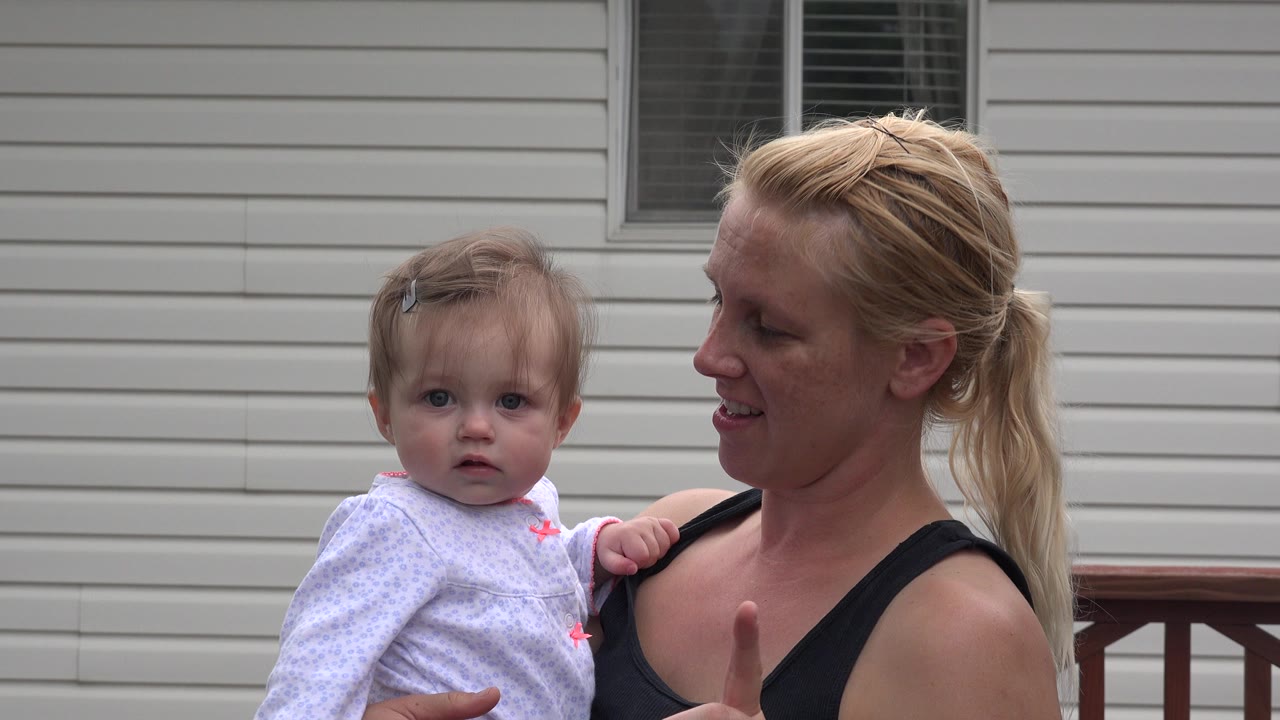 Mother holding baby in front of house siding.