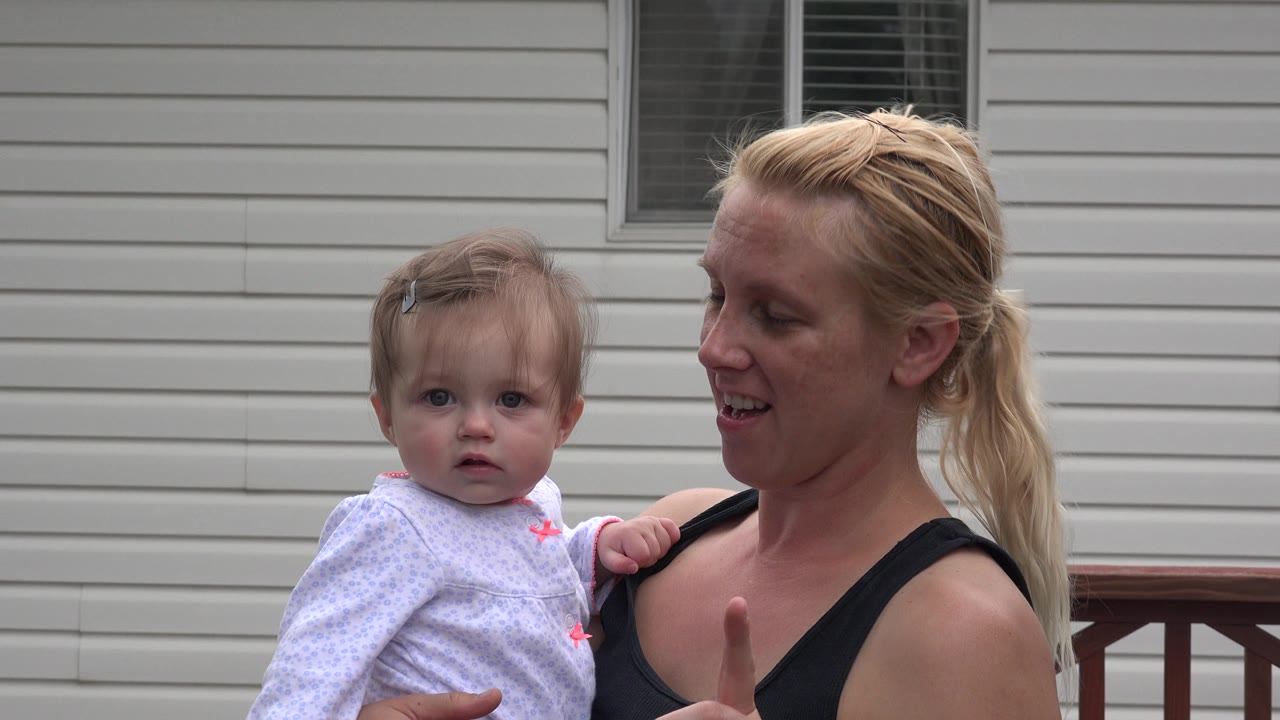 The mother turns toward the baby while holding her in front of pale siding and a window in Westminster, Colorado.