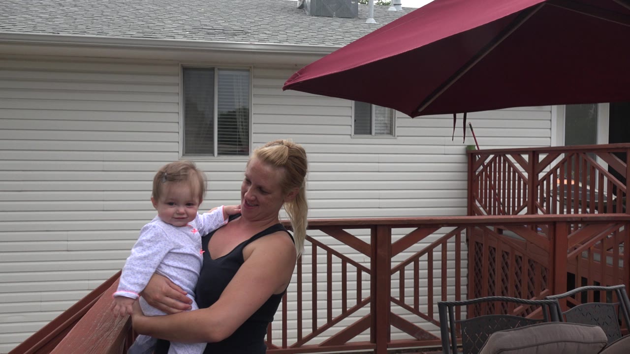 Mother holding a young child on a backyard patio deck.