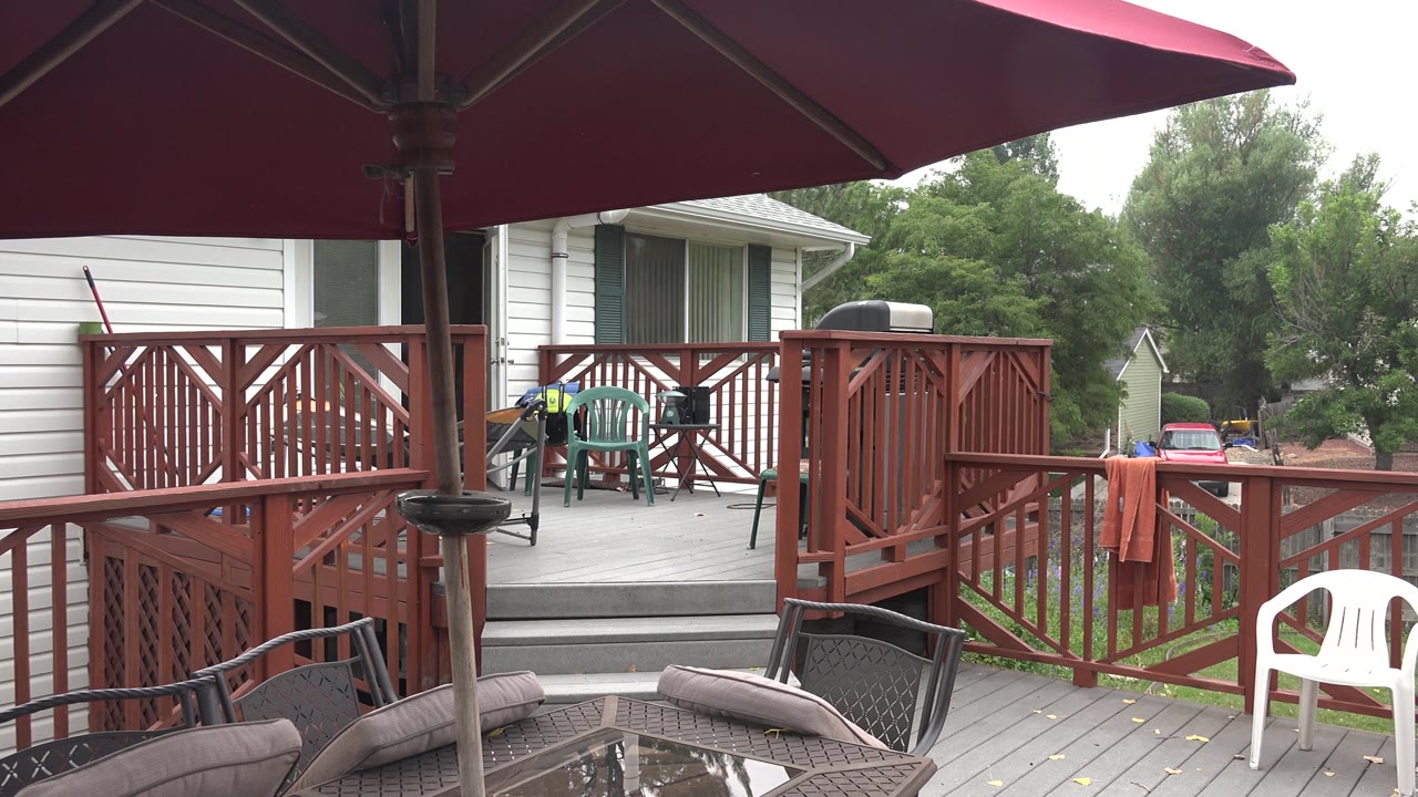 Backyard deck with red railing, umbrella, patio table, and white chairs near a lawn.