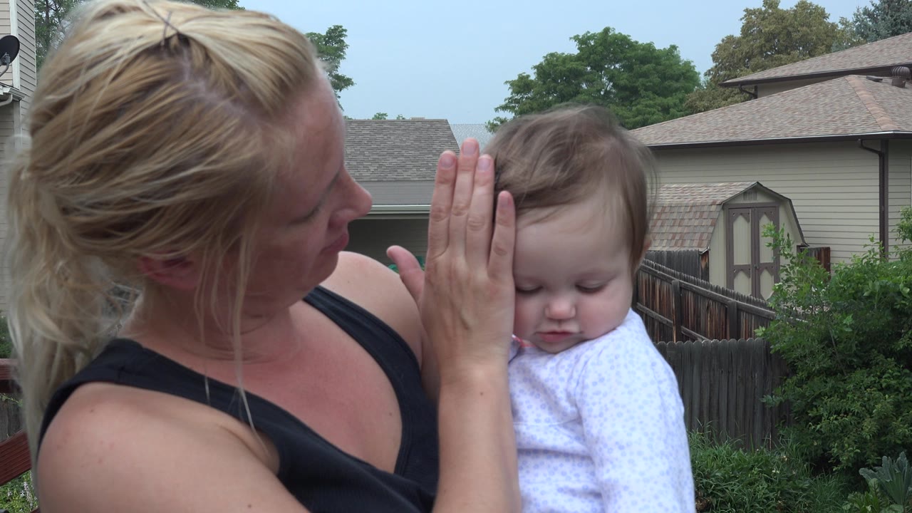 Mother holds her hand beside a baby outdoors.