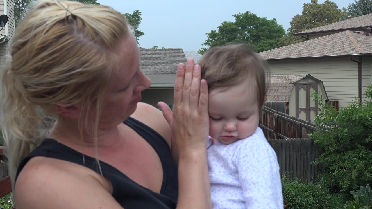 In Westminster, Colorado, the mother looks toward the baby while holding one hand upright near the child's face in the residential backyard.
