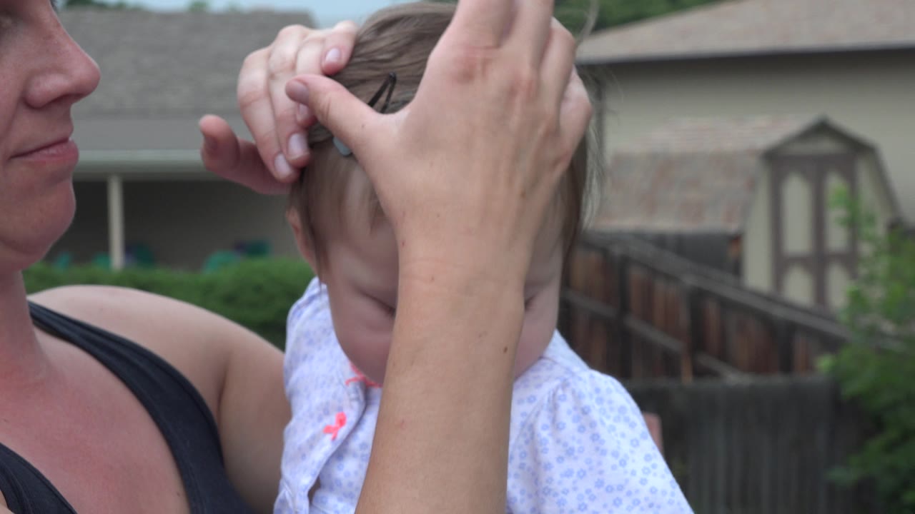 Woman holding a baby while hands cover the child's hair.