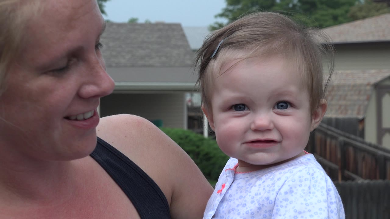 Toddler faces camera while mother smiles beside them.