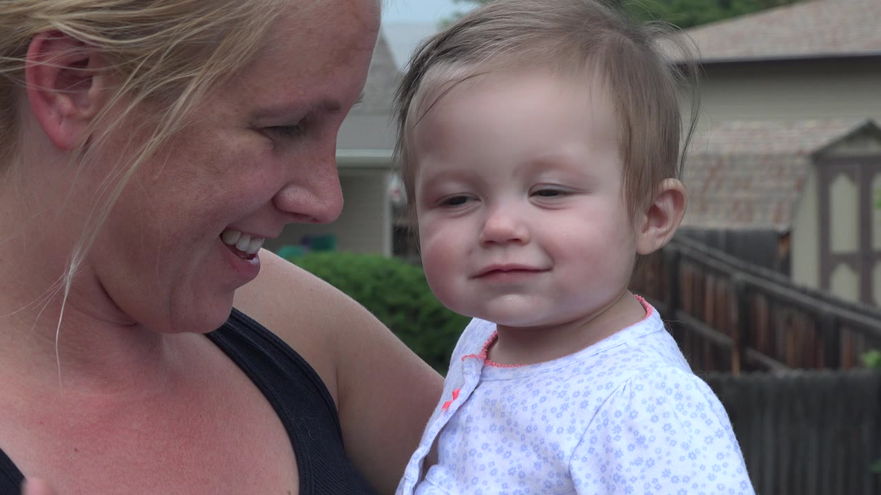 The mother looks down smiling as the baby girl faces forward in a close outdoor portrait in Westminster, Colorado.