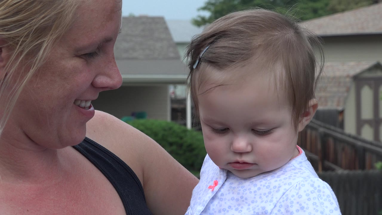 Baby girl looks down while mother smiles.