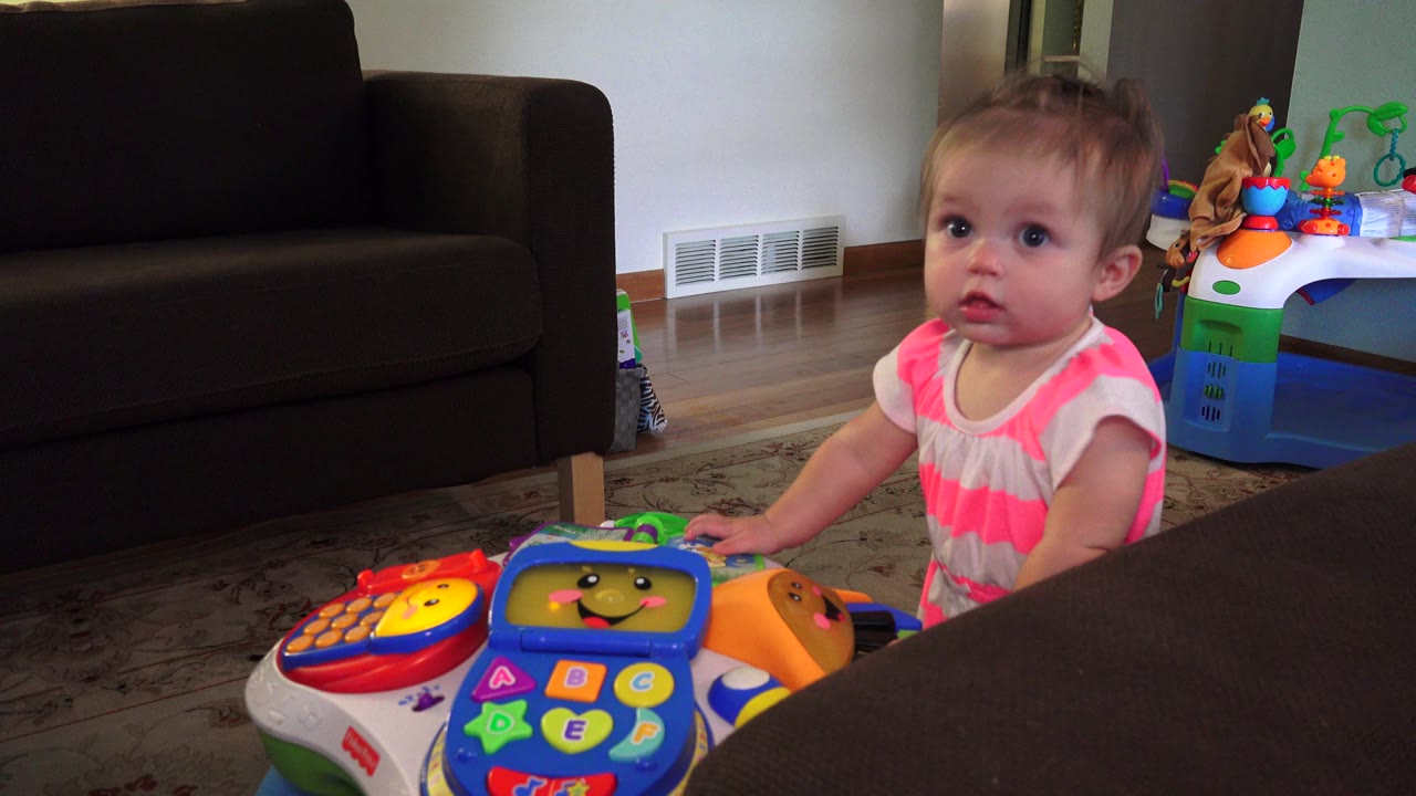 Toddler faces the camera while holding the edge of a colorful toy.