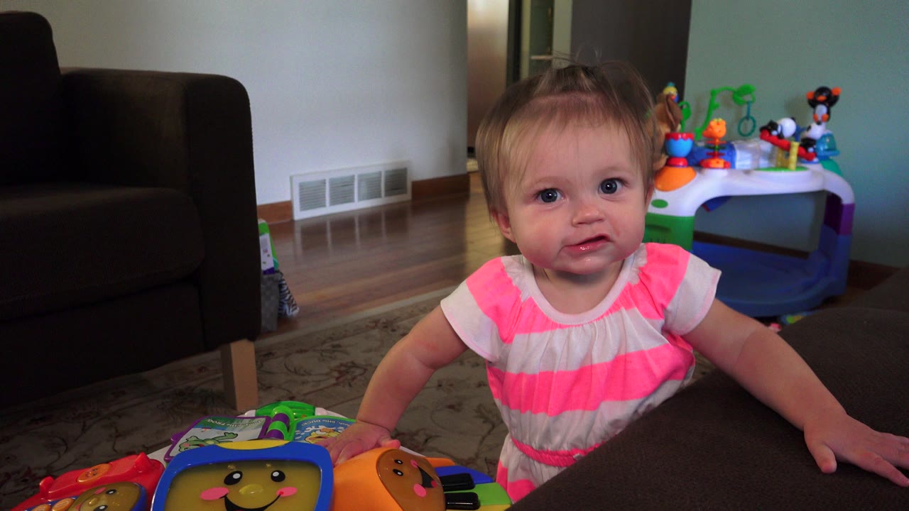 Toddler girl standing by a dark coffee table in a living room.