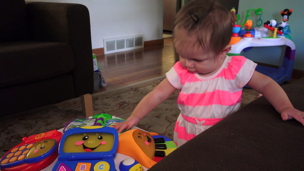 Toddler standing beside a couch and touching a colorful toy.
