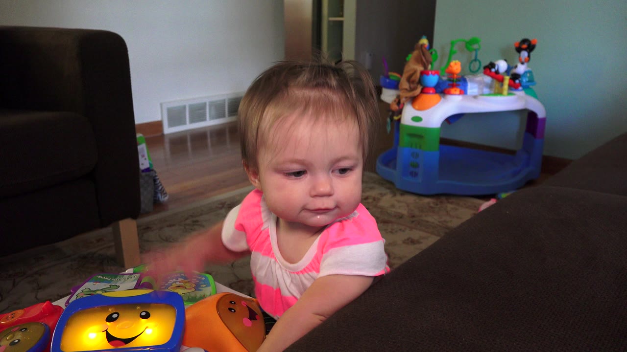 The toddler looks down toward the glowing face on the toy while standing beside the couch in the Westminster, Colorado home interior.