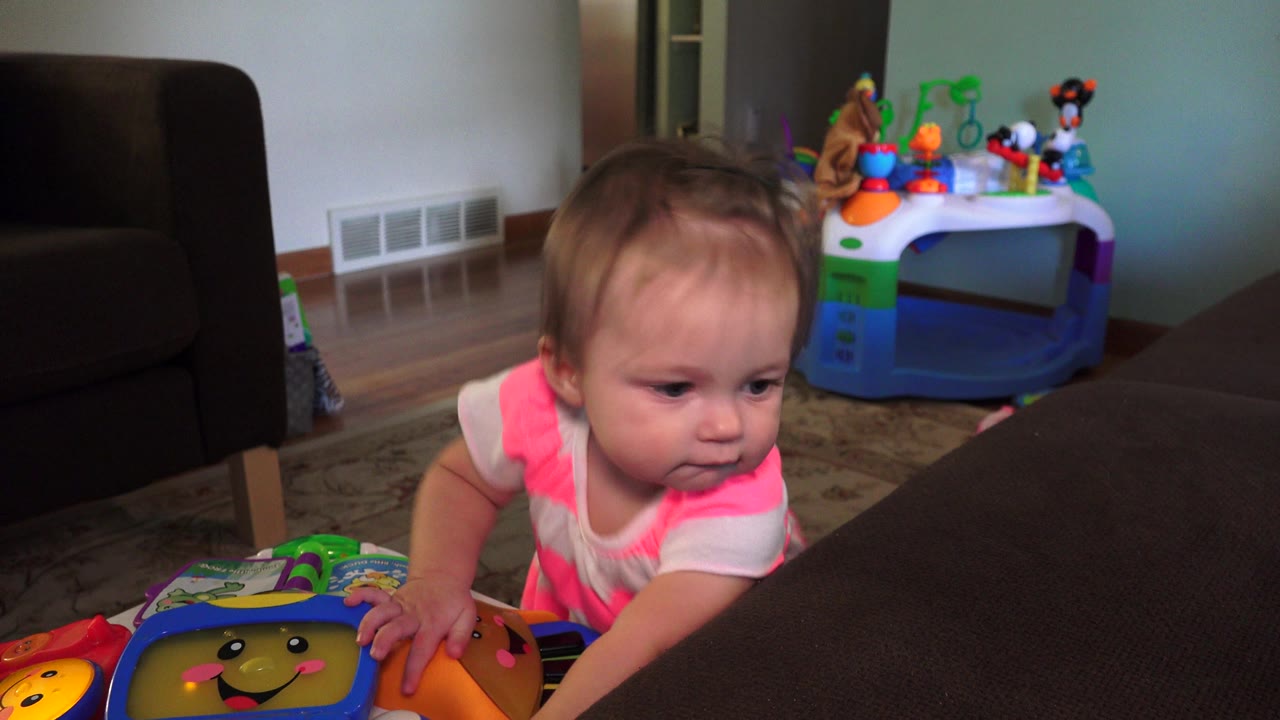 Toddler leans forward with one hand on a colorful toy by the couch.