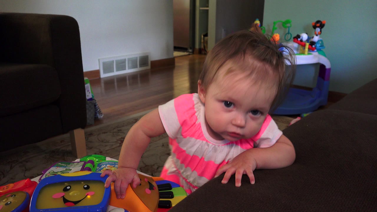 Toddler leaning over a colorful toy keyboard at a dark table.