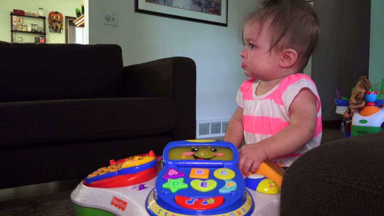 Young child beside a colorful toy table in a living room.