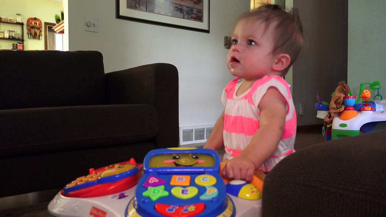 Baby standing beside a colorful activity toy in a living room.
