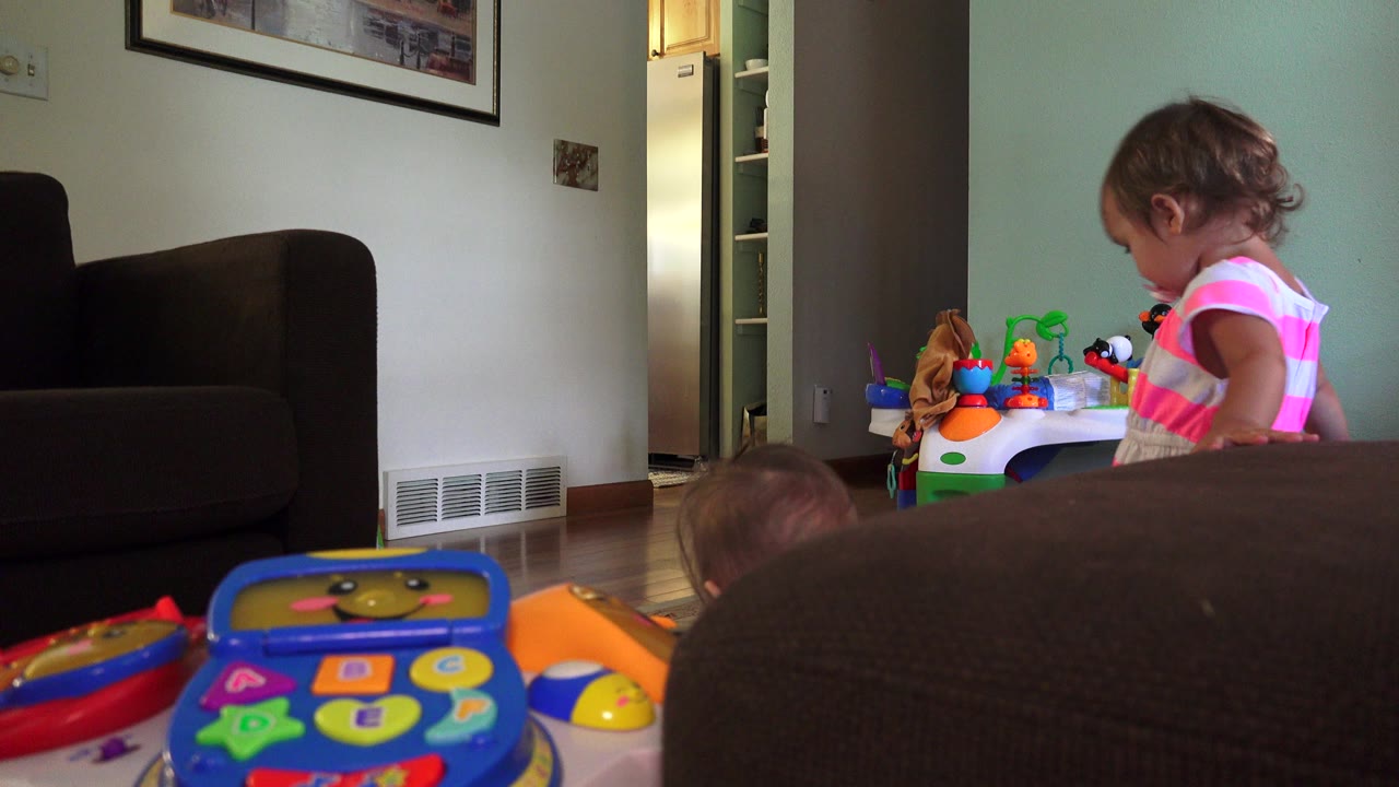 Toddler near a toy table in a living room with colorful toys in the foreground.