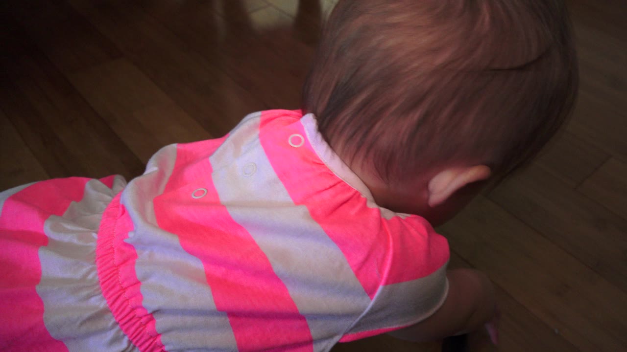 Baby girl in a pink striped outfit leaning over a wooden floor.