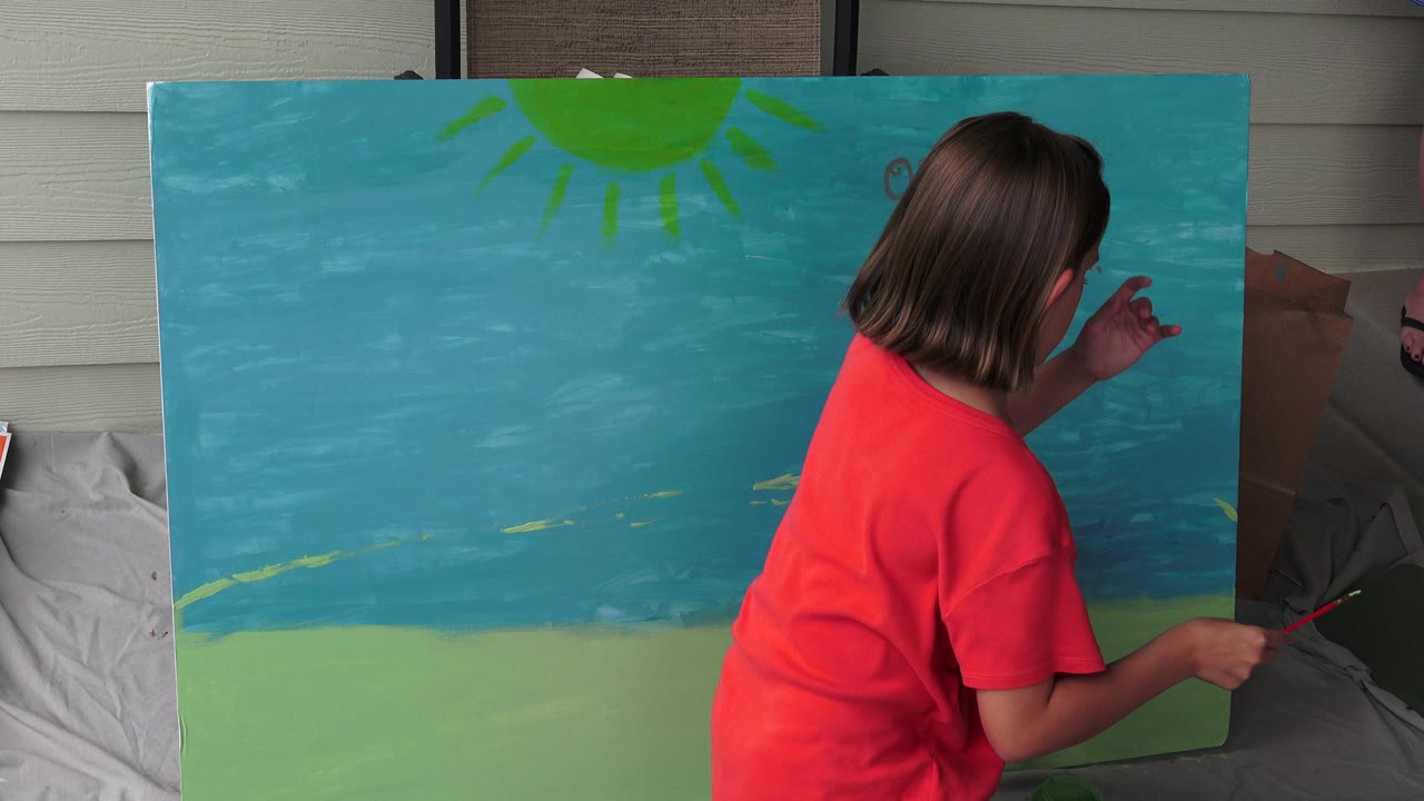In Broomfield, Colorado, the painter leans toward the right side of the blue canvas while holding a small brush, with the green lower section and sun still visible.