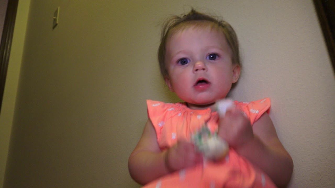 Toddler in coral outfit holding a small toy indoors.