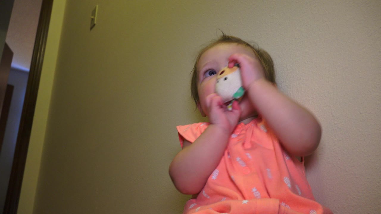 At 0:01 in Broomfield, Colorado, the baby keeps both hands around the white and green object, with their face partly covered and eyes looking upward.