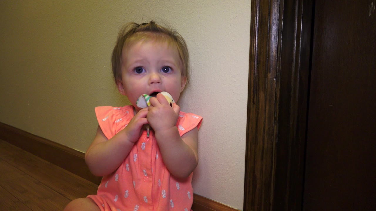 At 0:01, the child remains seated on the wood floor in Broomfield, Colorado, looking toward the camera with both hands around the toy.