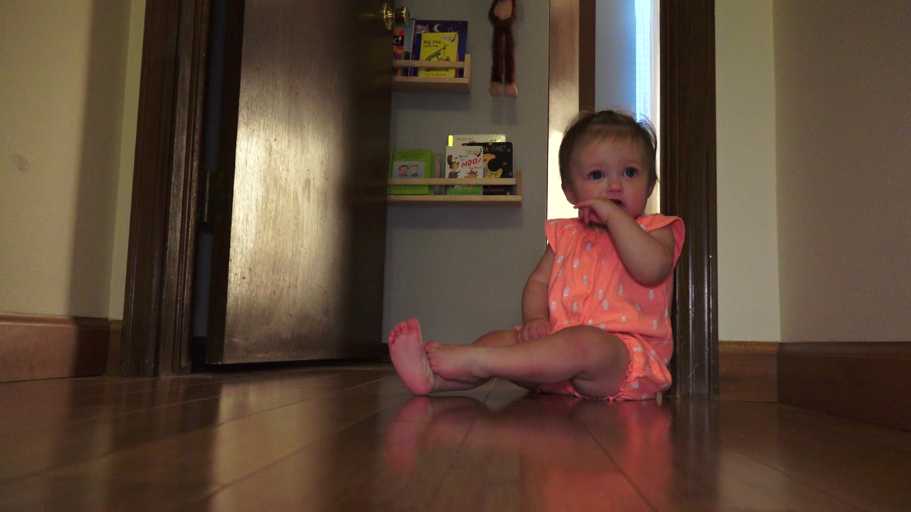 Baby girl sitting on a wood floor near an interior doorway.