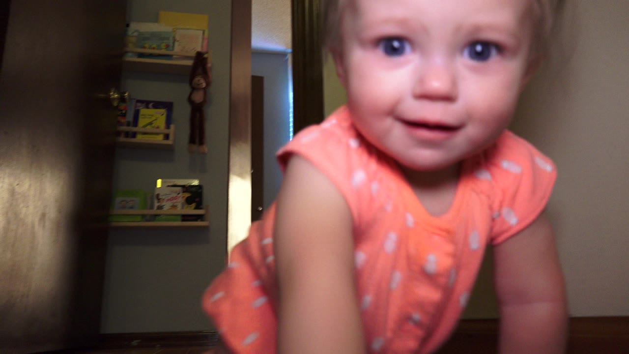 Baby in a coral onesie crawling toward a low camera indoors.