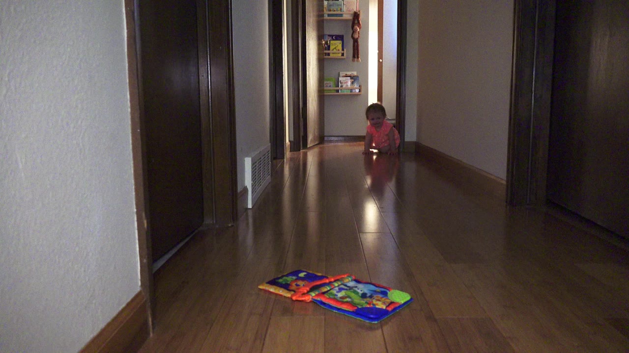 Toddler at the end of a hallway with a toy mat in the foreground.