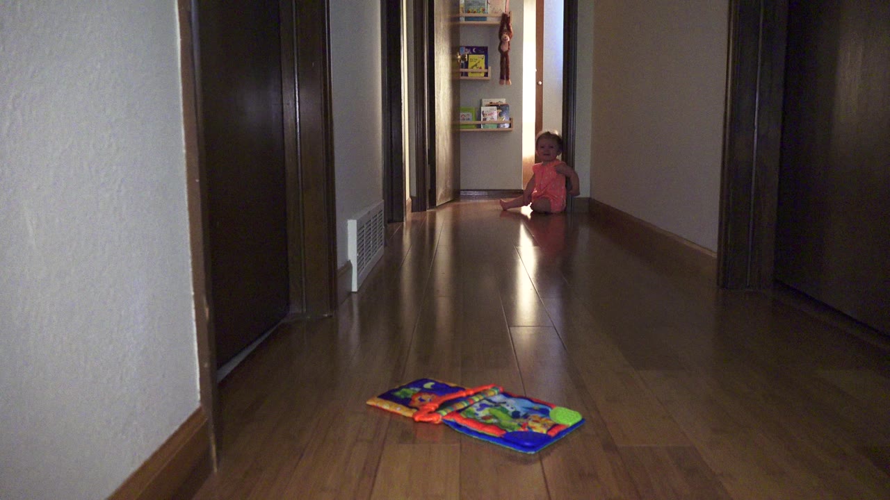 Young girl sitting at the end of a home hallway with toys in the foreground.