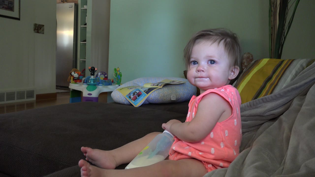 A baby in a coral outfit sits on a dark couch in a Broomfield, Colorado home interior, looking toward the camera with cushions and toys behind.