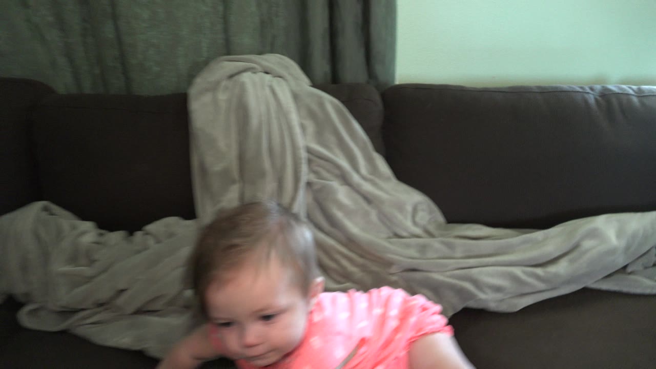 Baby partly visible at the bottom of a maroon couch with a grey blanket behind her.