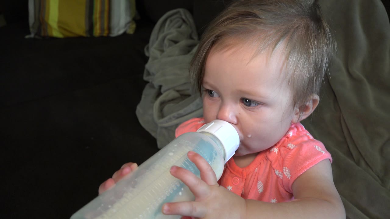 Toddler grips a partly translucent bottle close to her face.