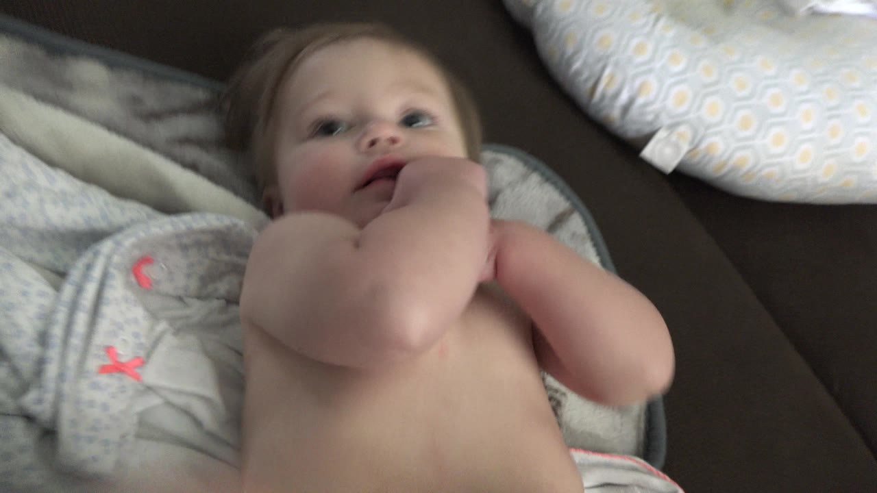 Baby lying on a towel with an adult hand near the mouth.