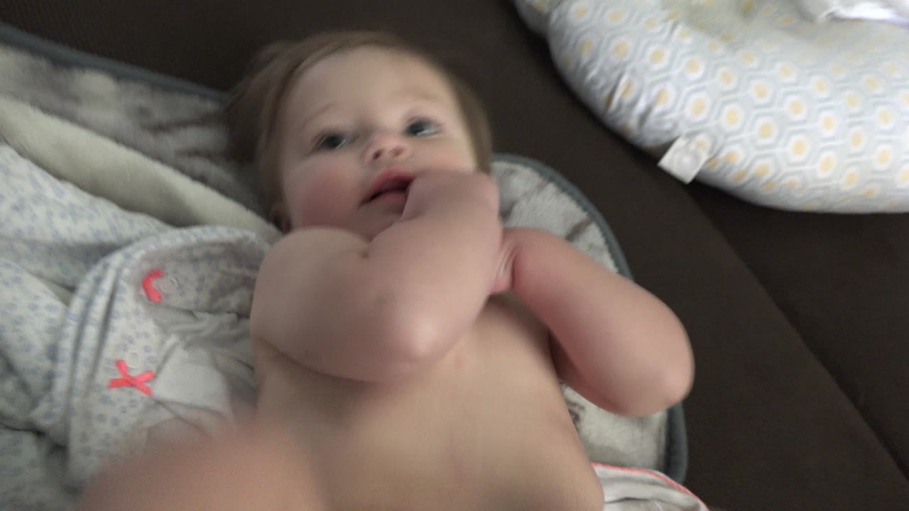 At 0:01 in Westminster, Colorado, the baby looks upward as an adult hand touches the child's cheek and mouth area on the towel-covered couch.