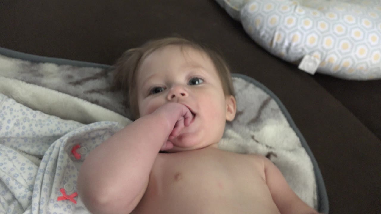Shirtless baby lying on a blanket with fingers in mouth.