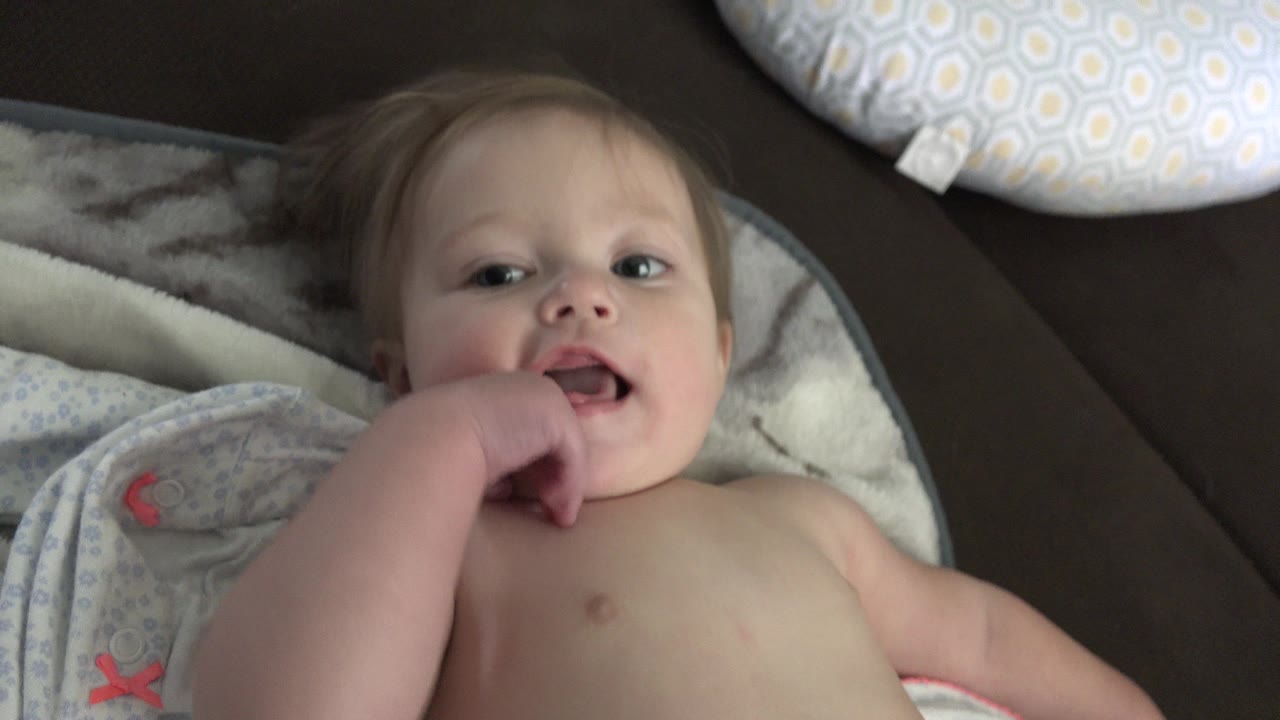 Toddler lying on his back with a hand near his mouth on bedding.