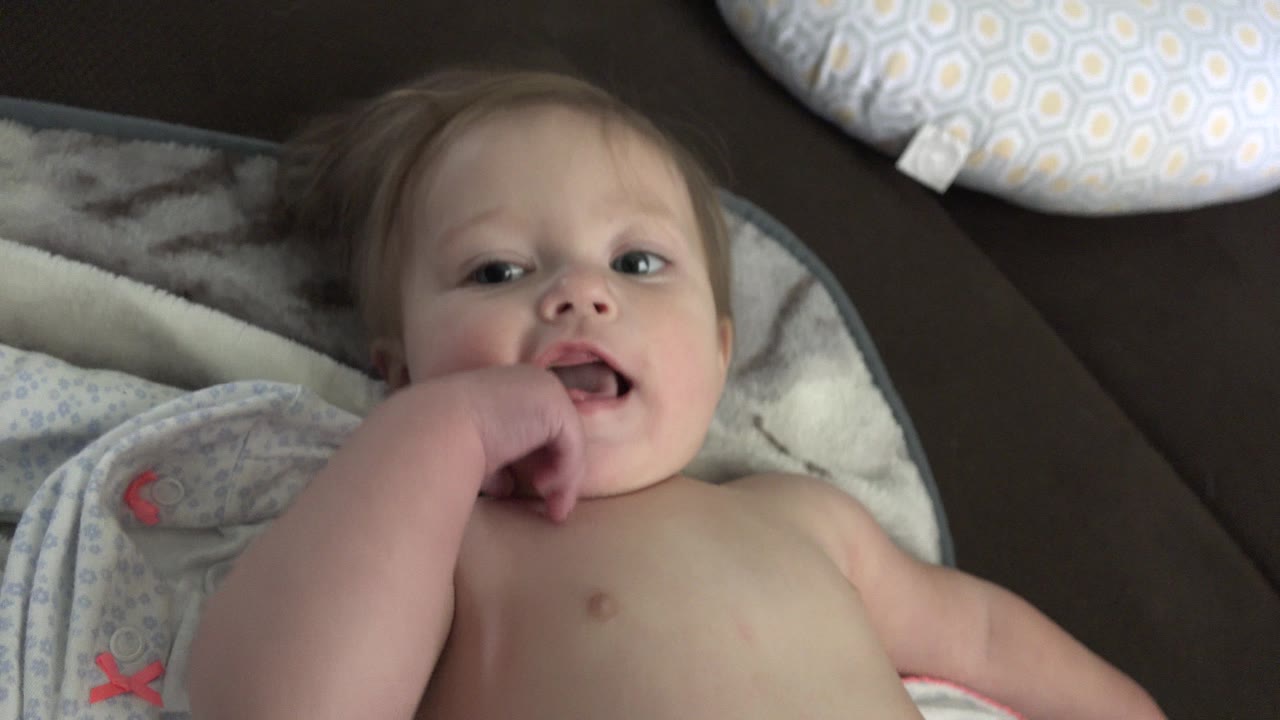 At 0:01, the toddler remains on his back in Westminster, Colorado, with fingers at his mouth and his face framed by blankets and a white patterned pillow.