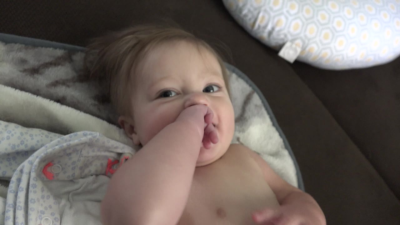 A toddler in Westminster, Colorado lies on patterned bedding with one hand in their mouth and a pillow visible above the head.